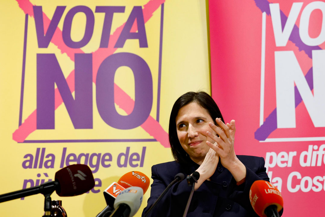 Die sozialdemokratische Oppositionsführerin Elly Schlein reckt die Hände zu einer siegessicheren Geste. Im Bildhintergrund Plakate, die dazu auffordern, beim Referendum über die italienische Justizreform mit „Nein“ zu stimmen.