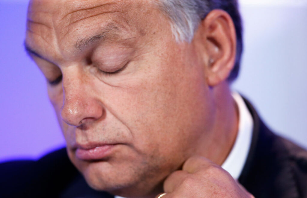 Nahaufnahme des ungarischen Ministerpräsidenten Viktor Orbán, der die Augen geschlossen hat und sich an den Hemdkragen fasst.