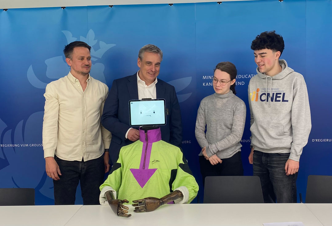 Jeff Kaufmann, von Bee Secure, Bildungsminister Claude Meisch (DP) und Vertreter*innen des Schüler*innenkommitees Cnel (v.l.n.r.) posieren mit Kampagnenmaskottchen „René“, einem Tablett mit Smiley Gesicht, das auf einem Holzkörper montiert wurde.