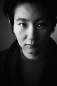 Portrait d’une femme en noir et blanc, cheveux noirs, le visage tourné vers l’appareil photographique.