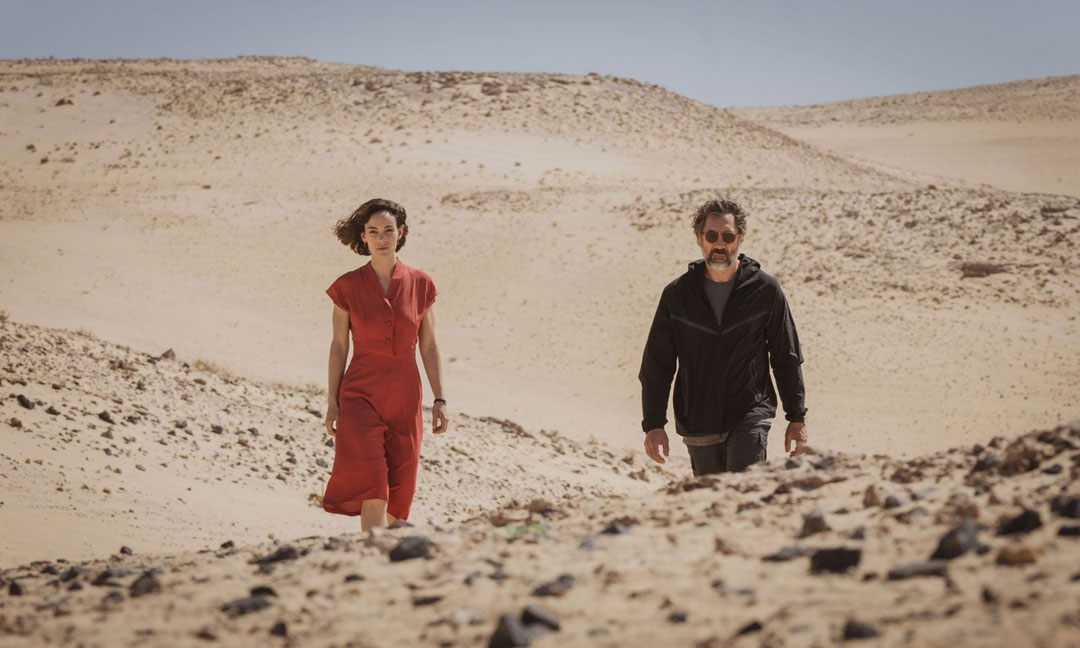 deux personnes, une femme a gauche et un homme a droite, marchent a travers un desert.