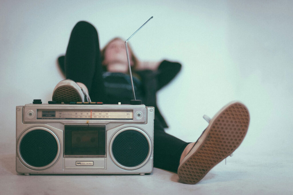 Ein Mensch, der entspannt auf dem Boden liegt. Die Füße zeigen in Richtung Kamera. Ein Fuß berührt ein Radio. 