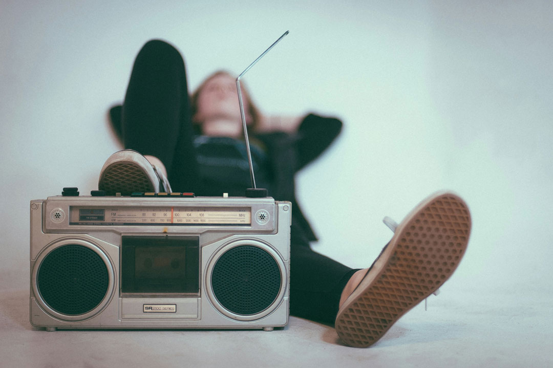 Ein Mensch, der entspannt auf dem Boden liegt. Die Füße zeigen in Richtung Kamera. Ein Fuß berührt ein Radio. 