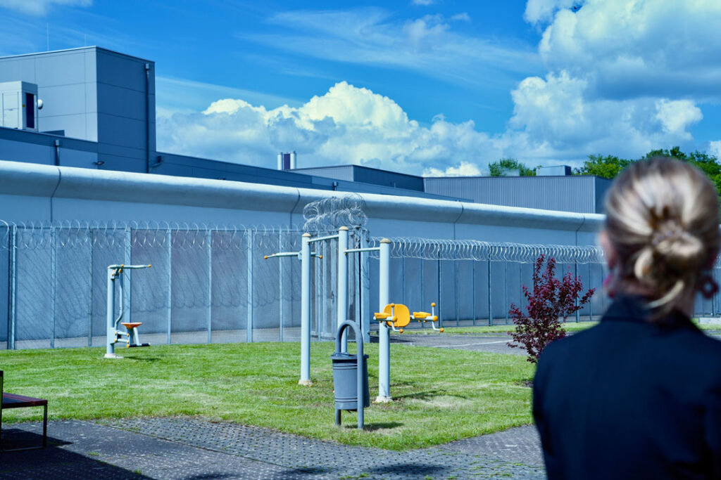 Aussenansicht des Gefängnis Schrassig mit dem Hinterkopf der Justizministerin Elisabeth Margue