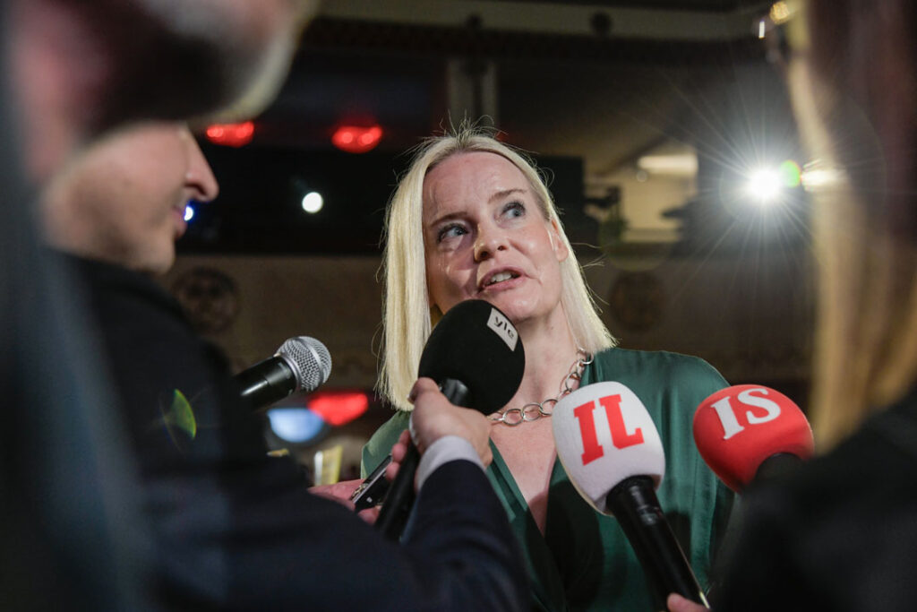 Die stellvertretende finnische Ministerpräsidentin und Finanzministerin Riikka Purra von den rechtspopulistischen „Die Finnen“ beim Interview, umgeben von Mikrofonen; die Gesichter der sie umgebenden Journalist*innen sind nur angeschnitten zu sehen.
