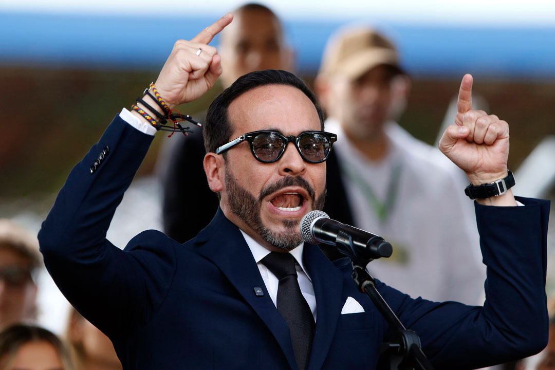 Der designierte kolumbianische Präsident Abelardo de la Espriella, in einen schwarzen Anzug gekleidet und mit Sonnenbrille, vor dem Mikrofon bei einer öffentlichen Rede unter freiem Himmel. Er hat beide Hände erhoben, streckt die Zeigefinger aus und gestikuliert. Hinter ihm sind schemenhaft Menschen zu erkennen.