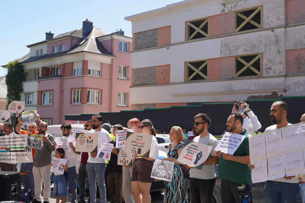 Un groupe de personnes se trouvent debout devant un bâtiment de bureaux, tenant dans leurs mains des pancartes.