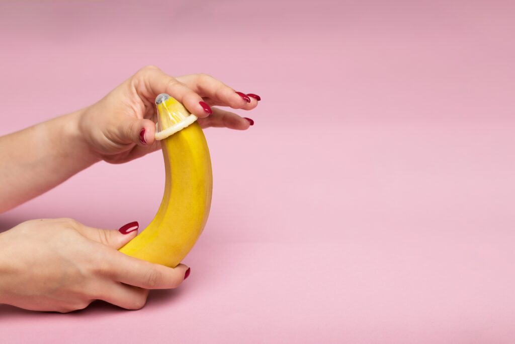 Eine Banane bekommt ein Kondom übergezogen.