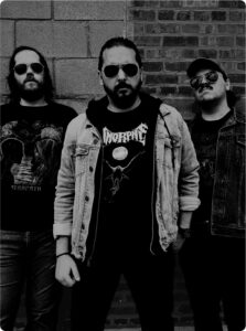 Schwarz-weißes Foto der Band Fer de Lance vor dem Hintergrund einer Hauswand. Die Musiker tragen Bandshirts und Sonnenbrillen.