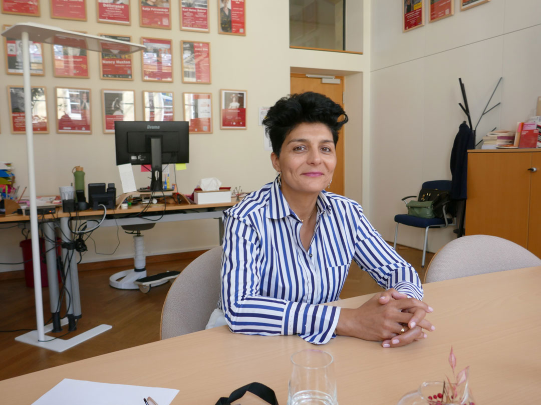 Portrait d’une femme accoudée à son bureau, cheveux courts et noirs