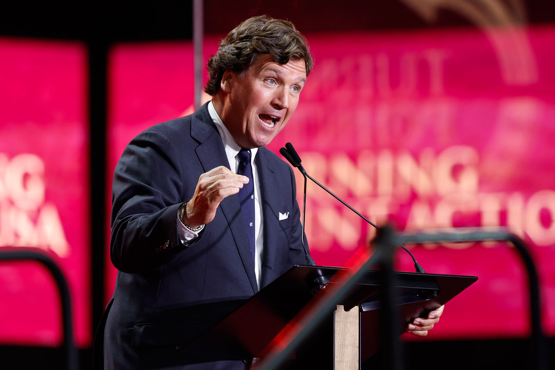 Tucker Carlson, mit einer Hand gestikulierend, die andere am Rednerpult.