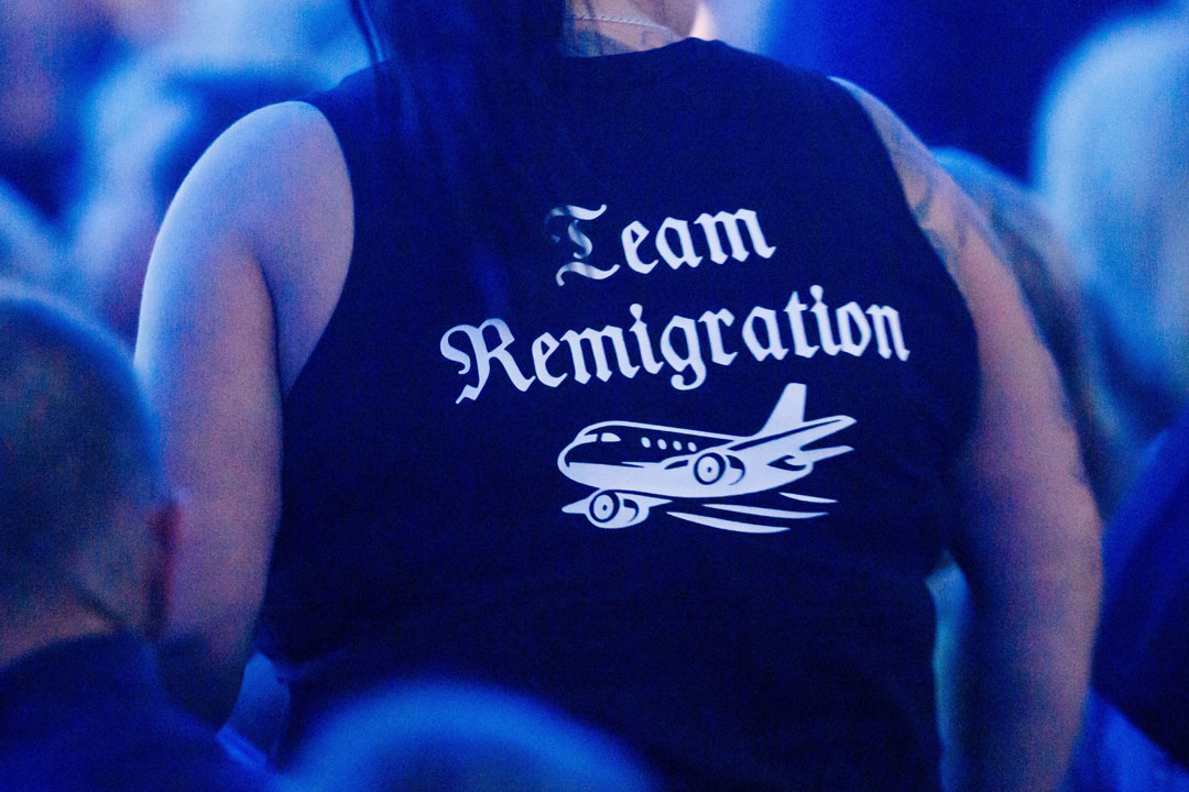 Eine Person von hinten fotografiert, die ein T-Shirt mit der Aufschrift „Team Remigration“ trägt. Unter dem Schriftzug ist die Zeichnung eines Flugzeugs abgebildet.