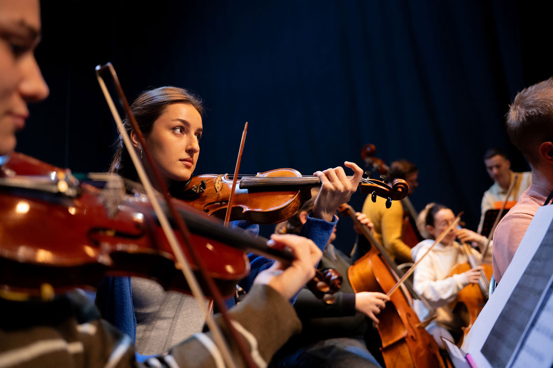 Eine junge Frau spielt Geige in einem Orchester.
