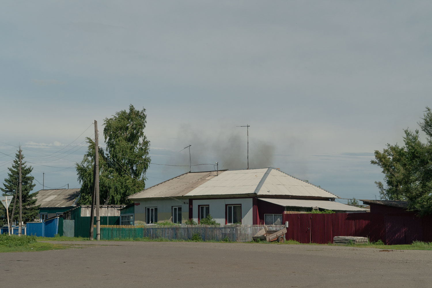 Deux maison blanches se profilent sur un ciel bleu. Derrière elles, se lève un nuage sombre de poussière.